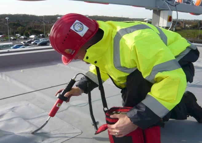 Surveyor in hi vis using electronic leak detection probe on a flat roof membrane